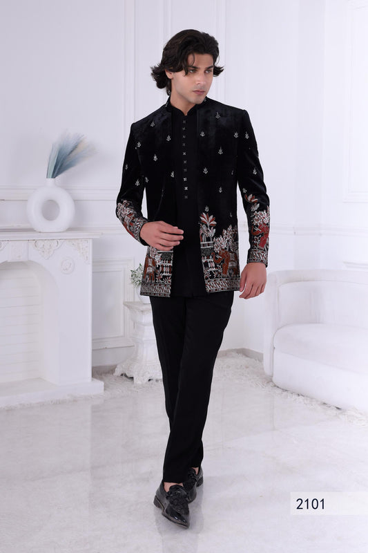 Man wearing a black embroidered traditional outfit in a white room.